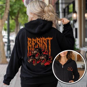 May include: Black hooded sweatshirt with a graphic of three black panther heads in flames with the word "RESIST" in a metal font above them.