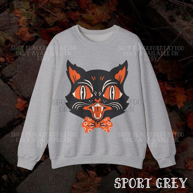 May include: Sport grey sweatshirt featuring a black cat face with orange eyes and a bow tie. The cat's mouth is open, revealing teeth. The text "SHOP BLACKFORDTATTOO ONLY AVAILABLE ON ETSY" is printed around the design. The words "SPORT GREY" are at the bottom.
