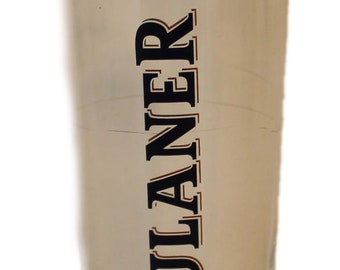 Op de afbeelding: Een hoog, helder bierglas met een uitlopende vorm en een afgeronde basis. Het glas heeft het "PAULANER MUNCHEN" logo in een cirkelvormig ontwerp en de merknaam verticaal afgedrukt.