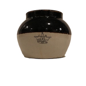 May include: A two-toned stoneware crock with a dark brown top and a light beige bottom. The crock features a crown emblem with the number "2" and the letters "qt" printed on the front. The jar has a rounded shape.