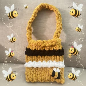 May include: A handmade yellow and black crochet bag with a handle. The bag features a bee design and is decorated with cartoon bees. The bag is made of a soft, textured yarn.