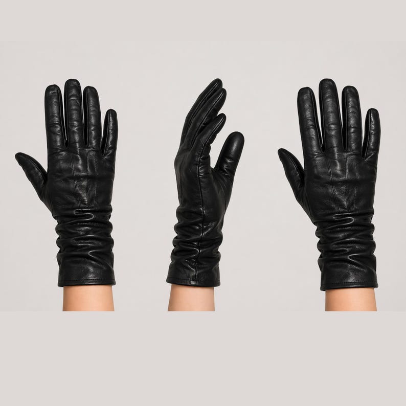 May include: A set of three black leather gloves shown from different angles. Each glove features a smooth finish, five fingers, and a gathered, ruched design at the wrist area. The leather has a slight sheen and visible natural texture throughout.