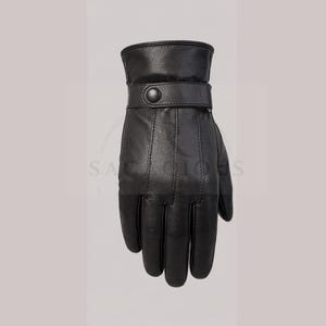 May include: A black leather glove featuring a wrist strap with a single snap button closure. The glove has visible vertical stitching along the back of the hand and fingers, with a smooth texture and a structured cuff design for a secure fit.