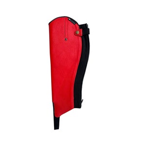 May include: A single red equestrian half chap with a black back panel. The red portion is made of a textured material and features a snap closure and a small strap. The black panel has a zipper.