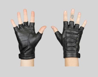 May include: A pair of black fingerless leather gloves. The left glove shows a smooth palm side with horizontal stitching. The right glove displays the back side featuring three horizontal perforated leather straps secured with small metal studs.