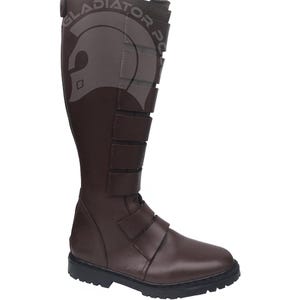 Puede incluir: Bota alta de cuero marrón con múltiples correas y suela negra. La bota presenta el texto "GLADIATOR PO" y un gráfico en la caña superior. La bota está diseñada con una puntera redondeada y un tacón resistente.