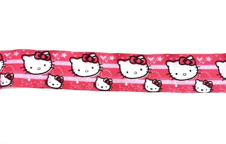 May include: Pink ribbon with a repeating pattern of white Hello Kitty faces with red bows. The ribbon has a white background with pink stripes and a white polka dot pattern.