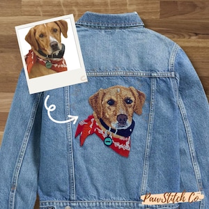 May include: Pale blue denim jacket with a detailed embroidered patch of a dog wearing a red bandana and a black collar. A polaroid-style image of the dog is in the upper left corner. The jacket has a classic design with a button-up front.