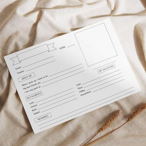 Pode incluir: Uma folha de memória escolar em branco para preencher com seções para "Sobre mim", "Meus favoritos" e uma foto. A folha inclui solicitações para o ano, a escola, o professor e a assinatura. A folha está em um tecido bege.