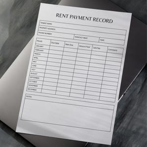 May include: A white "Rent Payment Record" form with black text, including fields for tenant information, monthly rent, and payment details. The form is on a dark gray surface.