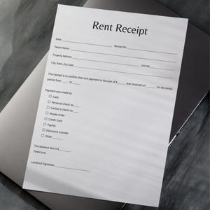 Puede incluir: Un recibo de alquiler blanco con el título "Rent Receipt" impreso en negro. El recibo incluye campos para la fecha, el nombre del inquilino, la dirección de la propiedad y los detalles del pago. El recibo está sobre una superficie gris.