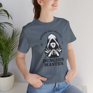 May include: A dark blue t-shirt with a white graphic of a hooded figure with the text "Beware the Smiling Dungeon Master".