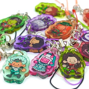 Peut inclure: Une collection de breloques en acrylique colorées représentant des personnages de dessins animés. Chaque breloque est d'une couleur différente, notamment vert, violet, rose et rouge, et possède un porte-clés argenté et un cordon de couleur assortie. Les breloques sont de style dessin animé.