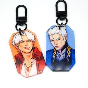 May include: Two acrylic keychains featuring anime-style portraits of men with white hair and green eyes. One keychain has an orange background and the other has a blue background. Both have black metal clasps.
