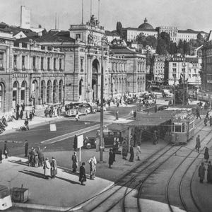 May include: A black and white photograph of a busy city square featuring neoclassical architecture, a large arched building, tram tracks, and a streetcar. Numerous pedestrians walk along the pavements and streets, while vintage automobiles are parked.