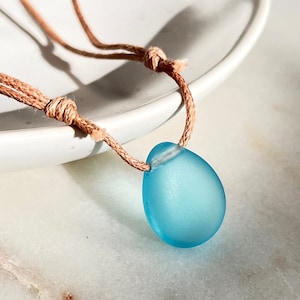 May include: A light blue sea glass pendant necklace on a brown cord.