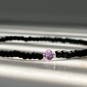May include: A delicate bracelet made with black beads and a single purple gemstone.