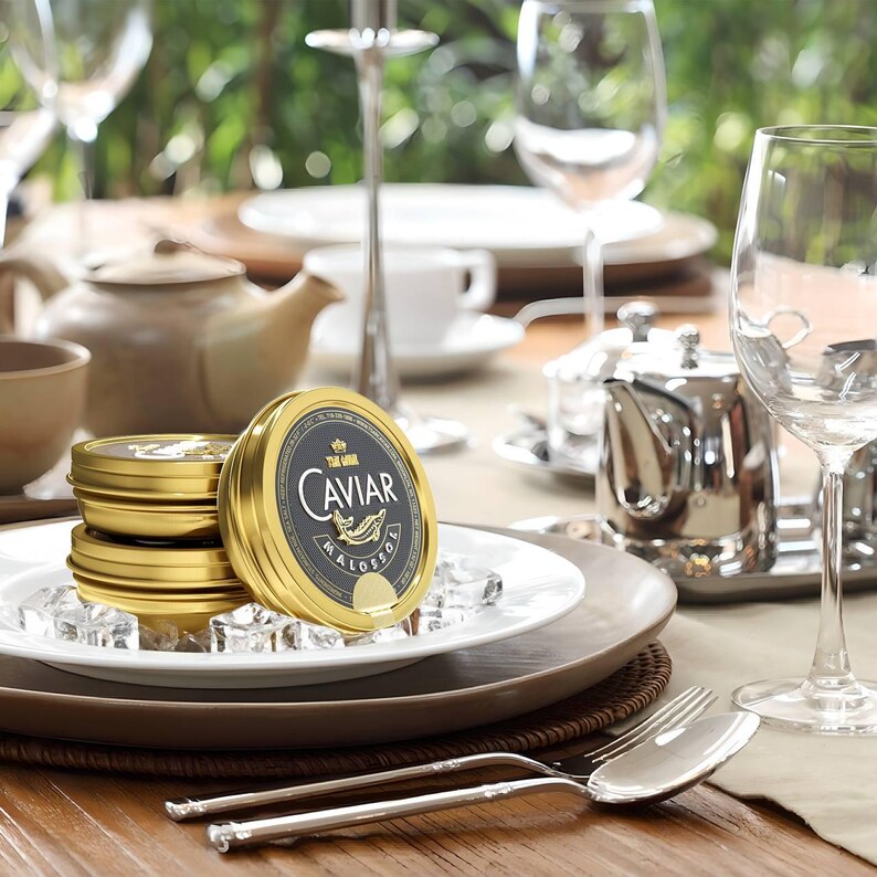 Puede incluir: Un juego de tres latas doradas de caviar en un plato blanco con cubitos de hielo. La lata superior tiene una etiqueta negra con la palabra "CAVIAR" en letras blancas y la palabra "MALOSSOZ" en letras blancas m&aacute;s peque&ntilde;as.