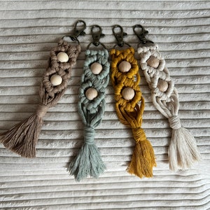 Puede incluir: Cuatro llaveros de macramé con cuentas de madera. Los llaveros son de color beige, azul claro, amarillo y blanco.