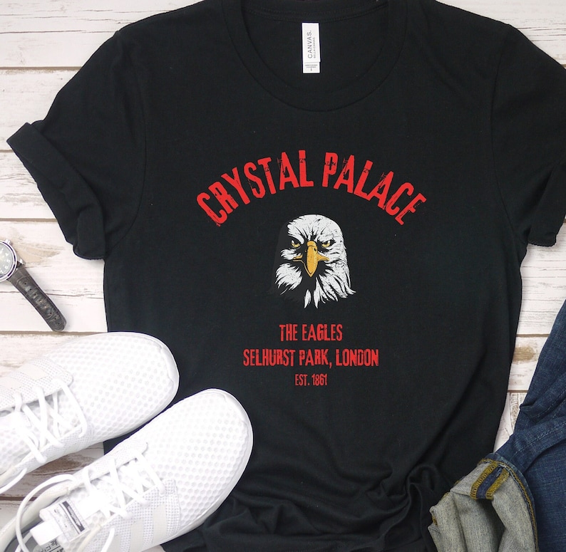 Puede incluir: Camiseta negra con un gr&aacute;fico rojo de un &aacute;guila y el texto "CRYSTAL PALACE THE EAGLES SELHURST PARK, LONDON EST. 1861"