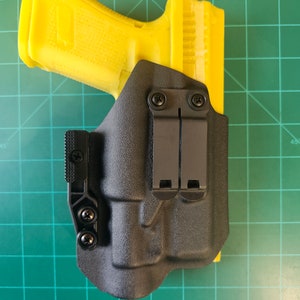 May include: A black polymer holster with a yellow polymer handgun inside. The holster has two adjustable clips and a screw-on attachment point.