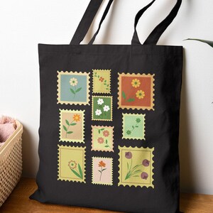 Peut inclure: Sac fourre-tout noir orné de motifs de timbres-poste floraux colorés. Les timbres présentent des fleurs jaunes, oranges, roses et violettes, sur des fonds vert clair et jaune. Le sac a des anses noires et est idéal pour le transport.