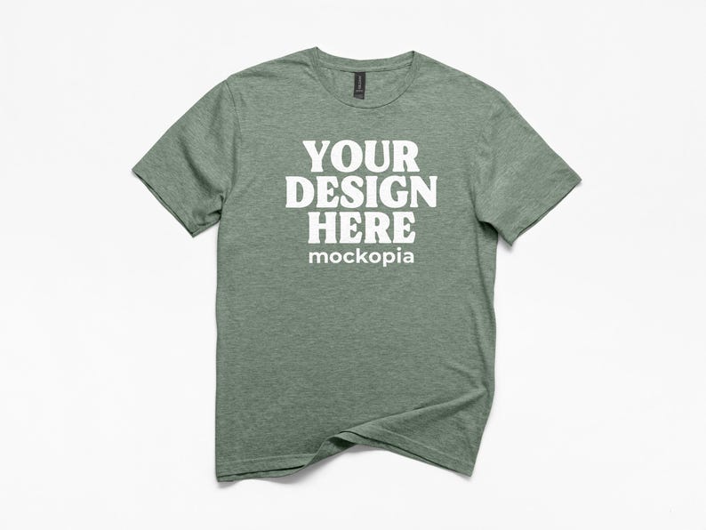 May include: A heather green t-shirt with the text "YOUR DESIGN HERE" in bold white letters. The word "mockopia" is below the main text. The shirt has a crew neck and short sleeves.