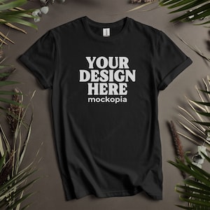 以下が含まれることがあります： 前面に白い文字で「YOUR DESIGN HERE mockopia」と印刷された黒いTシャツ