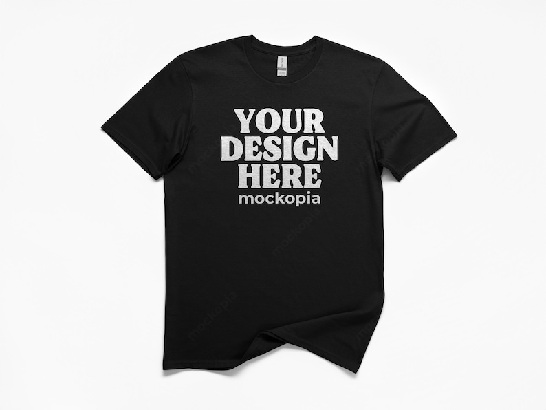 May include: Black crew neck t-shirt with the text "YOUR DESIGN HERE" in a bold, white font. The word "mockopia" is printed below the main text. The t-shirt is displayed on a white background.
