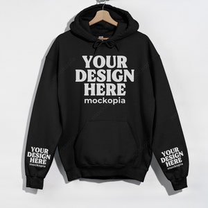 May include: Black hooded sweatshirt with the text "YOUR DESIGN HERE" and "mockopia" on the front and "YOUR DESIGN HERE" and "mockopia" on the sleeves.