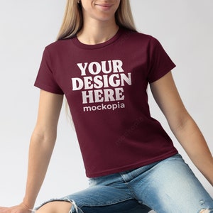 Può includere: Una maglietta color bordeaux con maniche corte e il testo "YOUR DESIGN HERE mockopia" stampato in bianco.