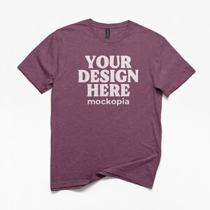 May include: A maroon crew neck t-shirt with the text "YOUR DESIGN HERE" in white block letters. The word "mockopia" is below the main text. The shirt is on a white background.