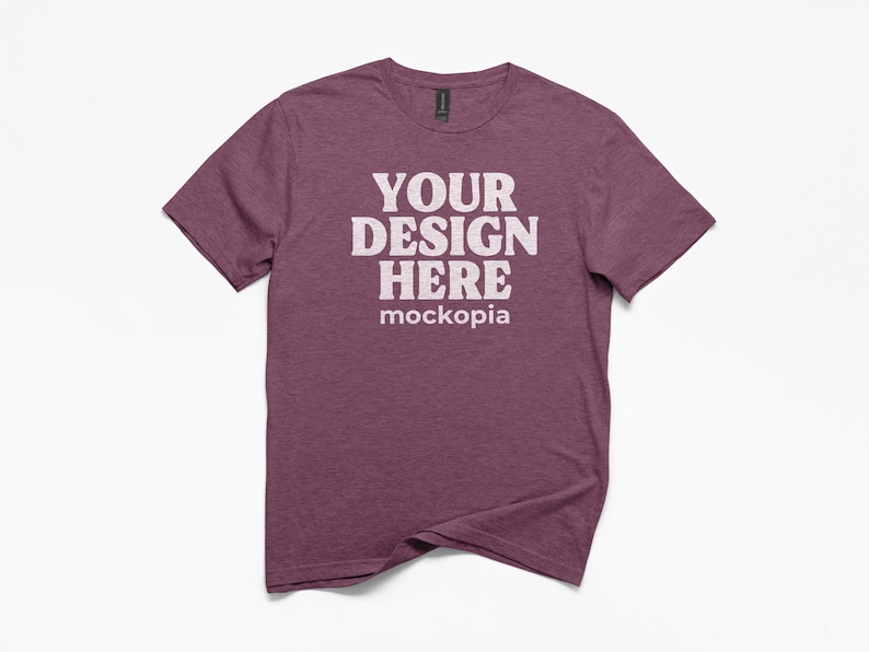 May include: A maroon crew neck t-shirt with the text "YOUR DESIGN HERE" in white block letters. The word "mockopia" is below the main text. The shirt is on a white background.