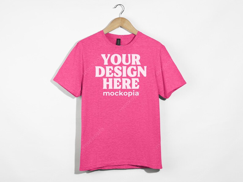 May include: Pink t-shirt with short sleeves and a crew neck. The shirt has the text "YOUR DESIGN HERE" and "mockopia" printed on the front.