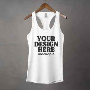K&ouml;nnte beinhalten: Wei&szlig;es Tanktop mit Racerback-Design. Das Tanktop hat den Text "YOUR DESIGN HERE" und "mockopia" auf der Vorderseite.