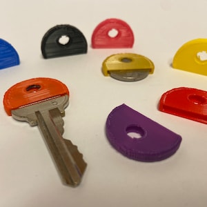 May include: A set of colorful key covers in various shapes, including half circles and a round shape. The key covers are made of plastic and have a hole in the center. A silver key with an orange key cover is also included.