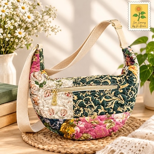 May include: A crescent-shaped quilted crossbody bag featuring a patchwork of floral patterns in shades of dark green, pink, yellow, and cream. The bag includes a beige adjustable canvas strap, a gold-tone metal zipper, and a top-stitched finish.
