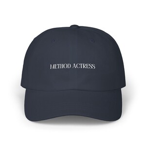 May include: A navy blue baseball cap with the text "METHOD ACTRESS" in white, centered on the front. The cap has a curved brim and a classic six-panel design.