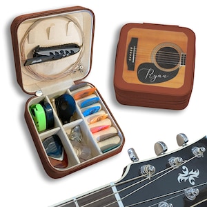 May include: A brown guitar accessory case with a zip, open to show guitar picks, a small knife, and guitar strings. A second case features a guitar design and the name "Ryan". A guitar headstock is in the foreground.