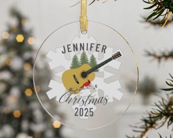 May include: Clear, round Christmas ornament with a gold ribbon. The ornament features a guitar, a red bird, and the text "Jennifer Christmas 2025". The background includes a white snowflake design and two green pine trees.