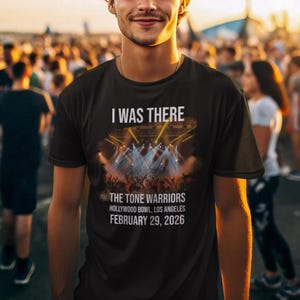 Könnte beinhalten: Schwarzes T-Shirt mit dem Text "I WAS THERE" über einer Konzertgrafik. Darunter steht "THE TONE WARRIORS HOLLYWOOD BOWL, LOS ANGELES FEBRUARY 29, 2026". Das T-Shirt wird von einer Person in einer Menschenmenge getragen.