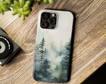 Op de afbeelding: Een smartphonehoesje met een aquarelillustratie van een mistig bos met donkergroene en blauwe dennenbomen tegen een bleke, mistige achtergrond. Het hoesje heeft een uitsparing voor een camerasysteem met drie lenzen in de linkerbovenhoek.