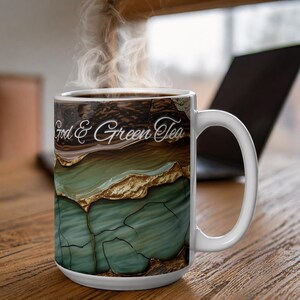 Könnte beinhalten: Weiße Keramiktasse mit dem Text "God & Green Tea". Die Tasse hat ein Design mit Braun-, Gold- und Türkistönen, das einer Geode ähnelt. Dampf steigt von der Oberseite der Tasse auf, was auf ein heißes Getränk hindeutet.