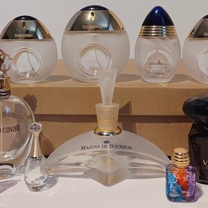 May include: A collection of perfume bottles, including Boucheron, Roberto Cavalli, Marina de Bourbon, and Versace Crystal Noir. The bottles are arranged on a brown surface.