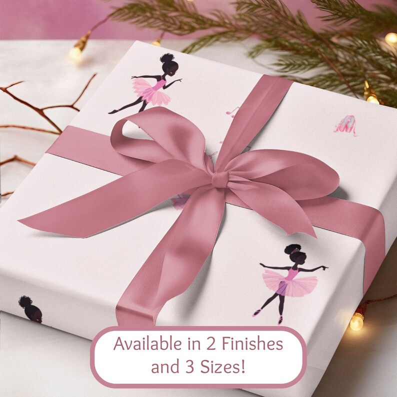 May include: A wrapped gift box with a dusty rose satin ribbon and bow. The white wrapping paper features illustrations of ballerinas in pink tutus. Text on the box reads "Available in 2 Finishes and 3 Sizes!"