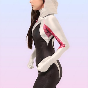 Puede incluir: Una mujer con un traje de spandex blanco y negro con una chaqueta con capucha blanca. El traje tiene un dise&ntilde;o de telara&ntilde;a en los brazos y el pecho. La mujer est&aacute; de pie con los brazos a los lados y la cabeza girada hacia un lado.