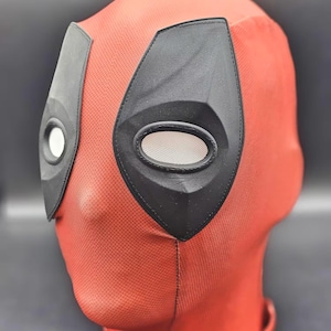 May include: Red and black Deadpool mask with eye holes and a textured surface.