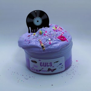 May include: Purple slime with glitter and colorful charms in a clear jar with a black record-shaped lid. The jar has a label that says "Guts".