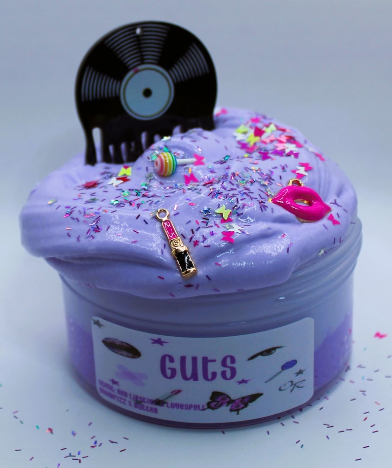May include: Purple slime in a clear jar with a black vinyl record, a pink lollipop, a gold lipstick charm, and pink and white glitter. The jar has a label that says "Guts" and "Lovespell".