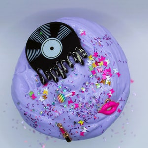 May include: Purple slime with glitter, a black vinyl record, a pink lipstick, a pink lollipop, and pink lips.